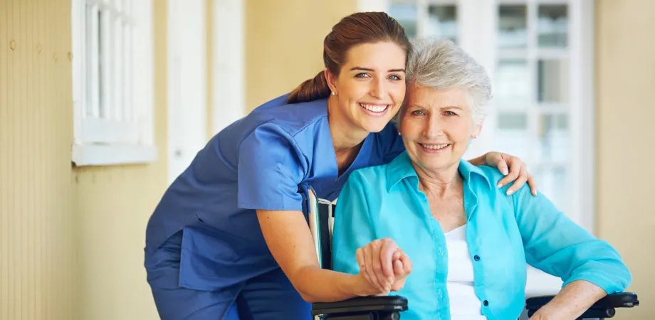 A caregiver smiling beside a client seated in a wheelchair on a porch