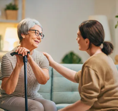An older woman with a walking cane talking and laughing with a companion on a sofa