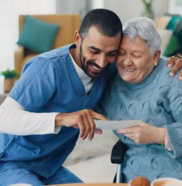 A caregiver and an older woman laughing together over a photograph